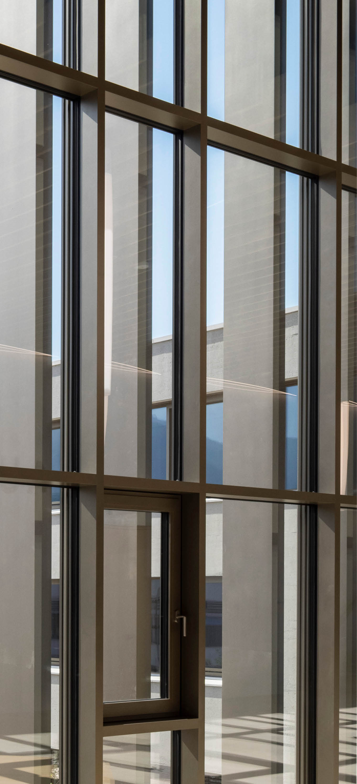Ein modernes Geb ude mit gro en Glasfenstern und einem ge ffneten Fenster in der Mitte, durch das man einen Innenhof mit weiteren Geb udeteilen sehen kann. Beschreibung von KI generiert