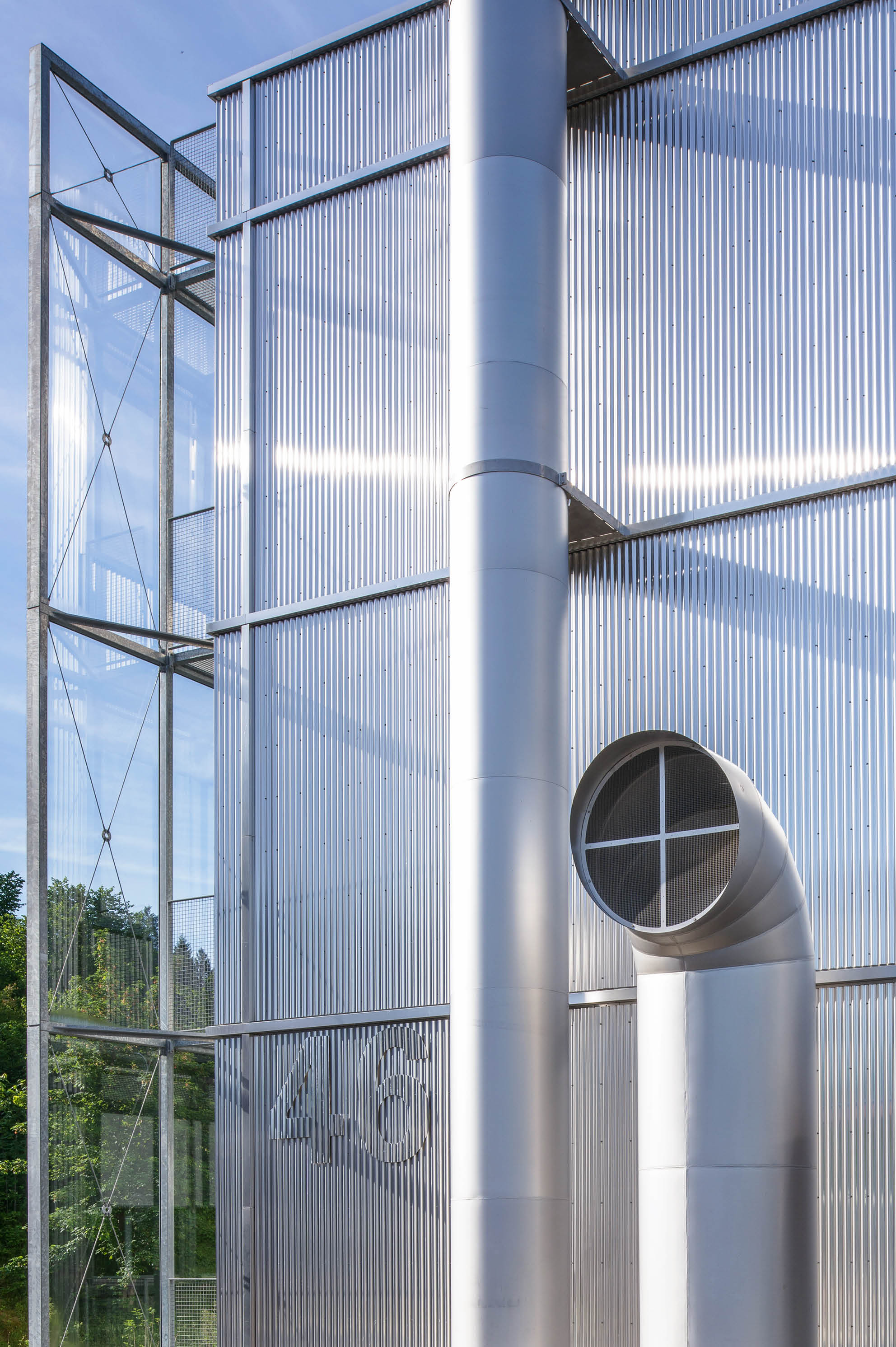 Ein modernes Industriegeb ude mit silbernen Metallw nden und gro en L ftungsrohren vor blauem Himmel. Beschreibung von KI generiert