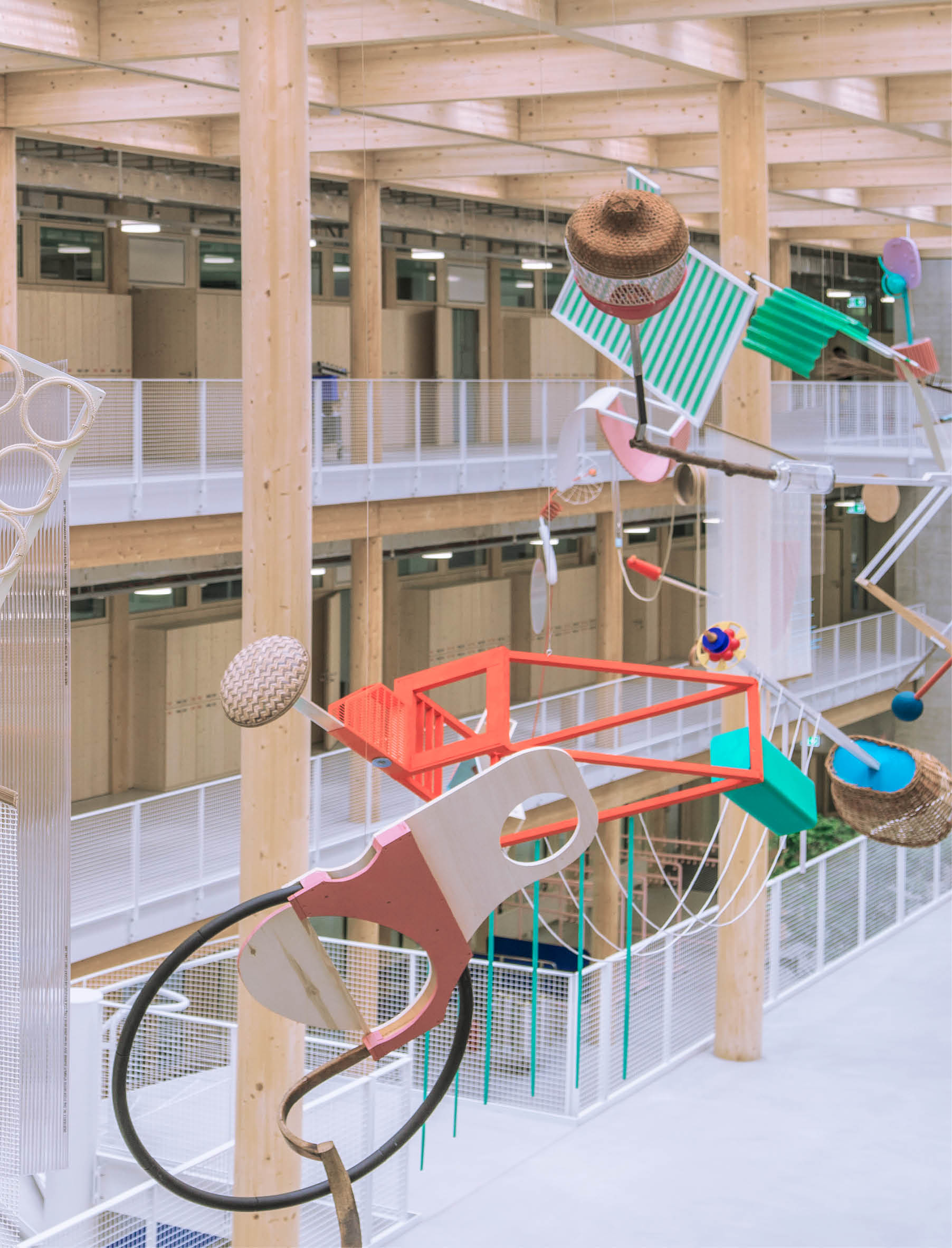 In einer modernen Halle h ngt eine farbenfrohe, abstrakte Skulptur aus verschiedenen geometrischen Formen, H ten und Alltagsgegenst nden, die an Seilen befestigt sind. Beschreibung von KI generiert