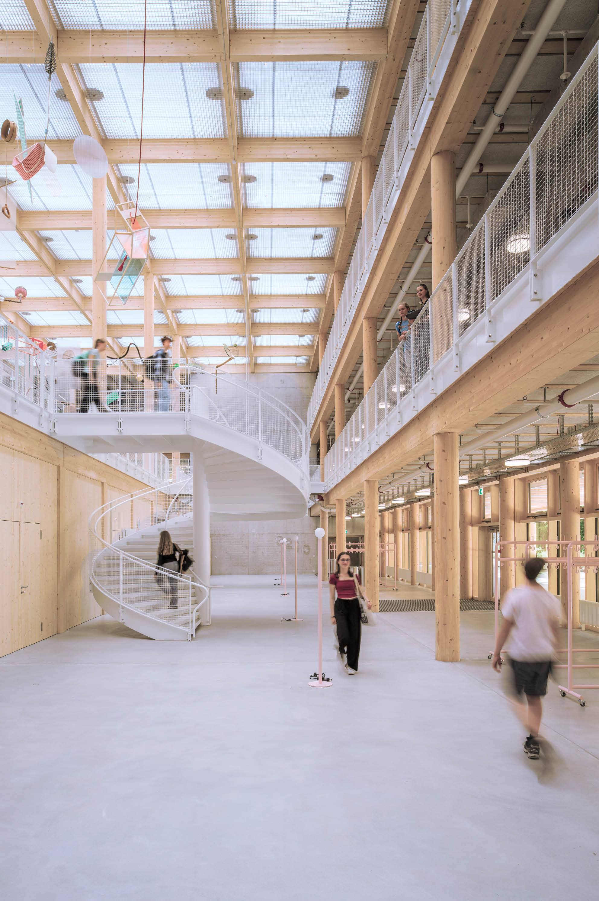 Helle moderne Innenraumhalle mit Holzst tzen, gro em Glasdach, einer wei en Wendeltreppe und mehreren Personen, die sich bewegen oder auf Balkonen stehen. Beschreibung von KI generiert